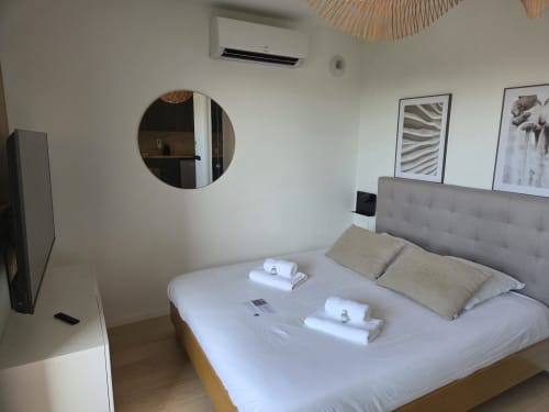 Chambre moderne de l'hôtel Les Loges De La Mer à Pérolles avec lit queen, tête de lit grise, miroir rond et climatisation