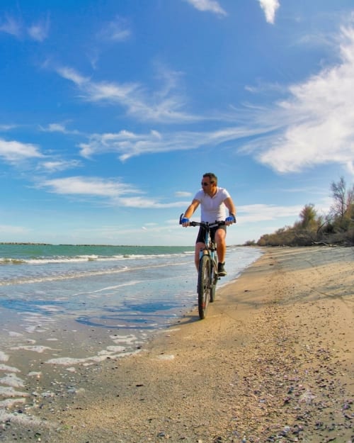 Uomo in bicicletta sulla spiaggia vicino a Casa Mia B&B a Porto Viro, Italia con mare turchese e cielo blu