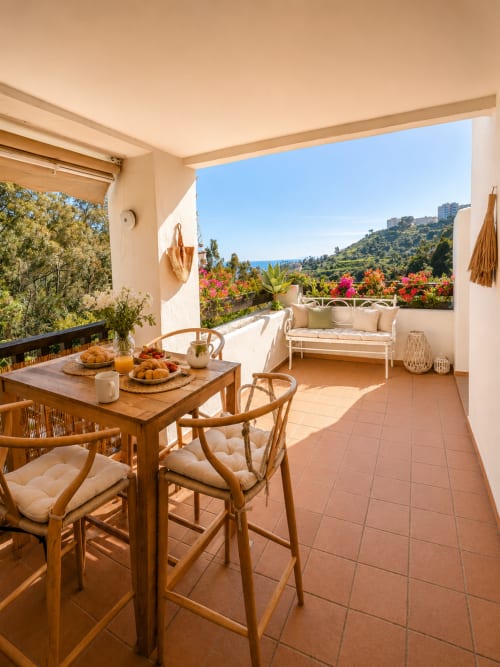 Terraza soleada en BH Marbella con mesa de comedor, vistas al mar, flores y paisaje costero