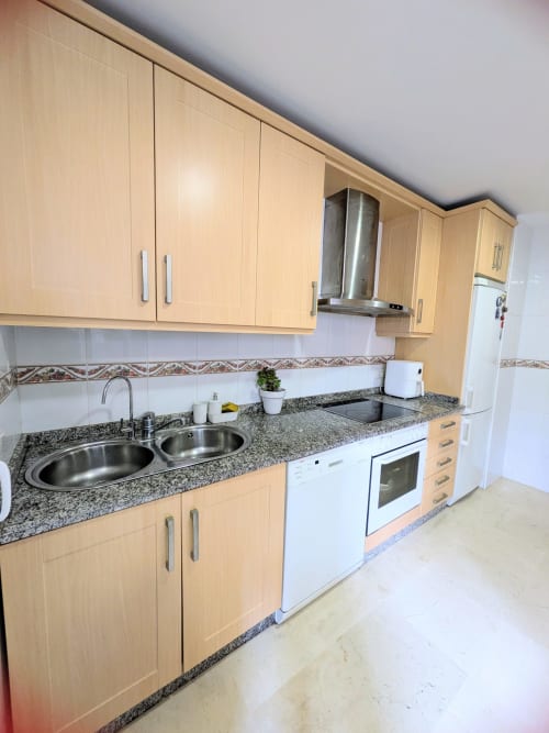 Cocina con madera clara, encimeras de granito, electrodomésticos de acero inoxidable y fregadero doble en el hotel BH Marbella