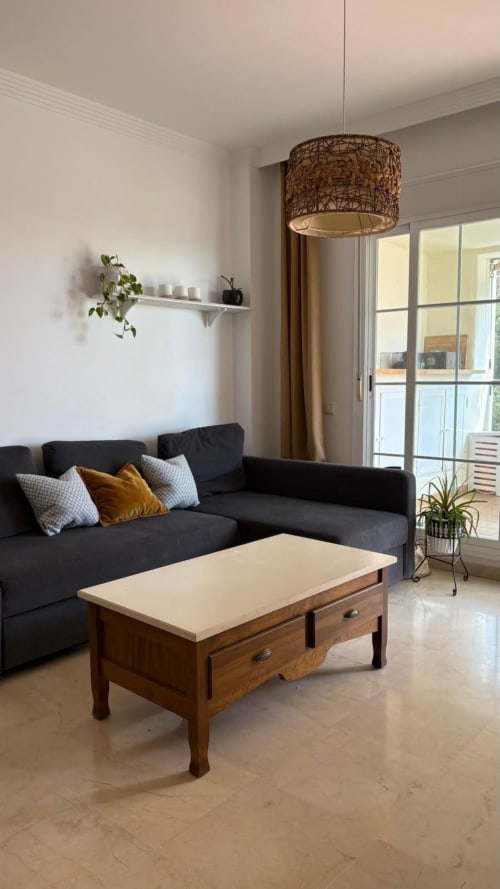 Moderna sala de estar del hotel BH Marbella con sofá oscuro, mesa de café de madera, lámpara colgante tejida y acceso al balcón