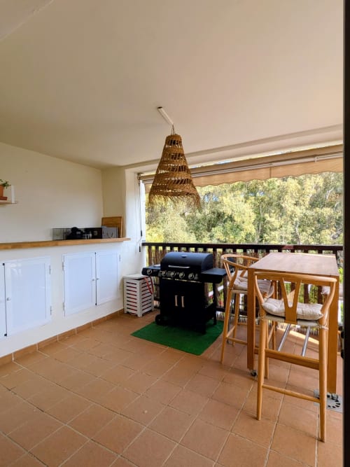 Terraza cubierta al aire libre en BH Marbella con parrilla BBQ, muebles de comedor y vistas al bosque