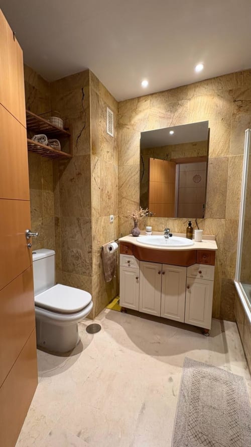 Baño moderno en BH Marbella con paredes de mármol, lavabo de diseño curvo, mueblería blanca e iluminación empotrada en Marbella,