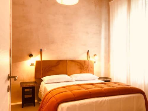 Camera matrimoniale accogliente con accenti in legno caldo, biancheria crema, plaid arancione, lampade a sospensione e finestra a Casa Città B&B a Brescia