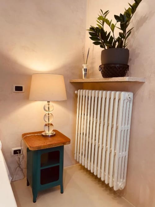 Accogliente angolo della camera Casa Città Brescia con lampada calda su comodino turchese e termosifone bianco sotto ripiano in legno con pianta