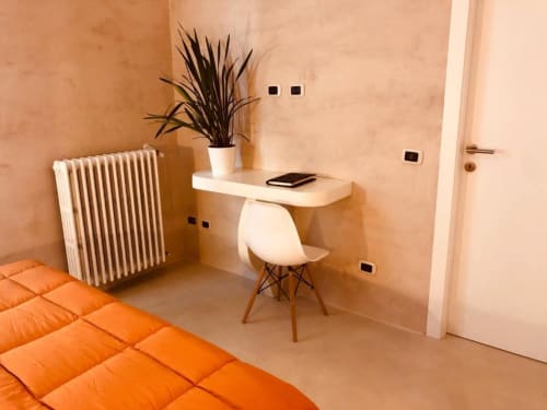 Moderno spazio di lavoro in camera doppia Casa Città Brescia con sedia bianca, pianta in vaso, radiatore e biancheria arancione