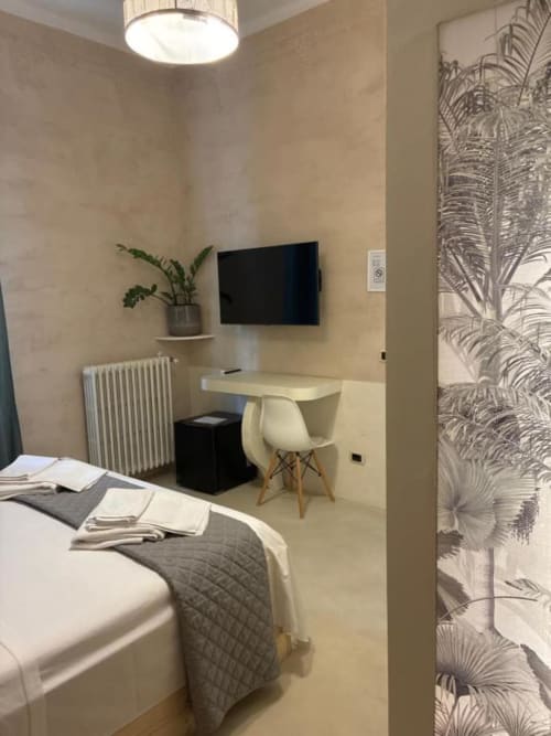 Camera matrimoniale moderna a Casa Città Brescia con letto, scrivania con sedia, TV a muro, pianta in vaso e carta da parati botanica