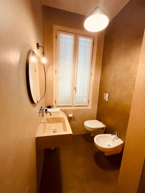 Bagno moderno di Casa Città Brescia con lavabo, wc, bidet, specchio rotondo e finestra con persiane