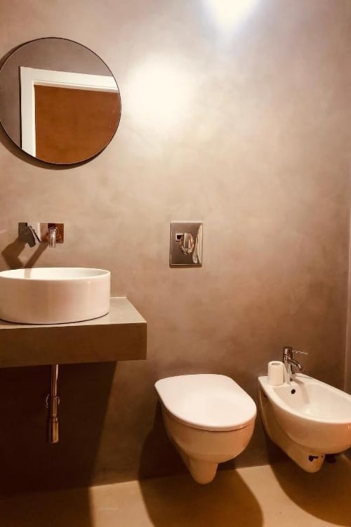 Bagno moderno a Casa Città a Brescia con specchio rotondo, lavabo in ceramica, wc, bidet e pareti dai toni caldi della terra