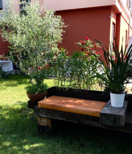 Area seduta in cortile di Casa Città Brescia con panchina, fiori in vaso e sfondo di edificio rosso