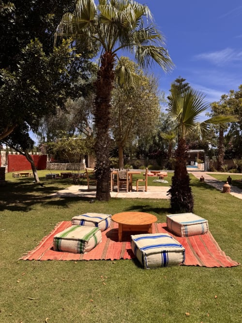 Salon extérieur avec coussins et table ronde dans un jardin verdoyant à l'Hôtel Ethnique Eucalyptus, Essaouira Maroc