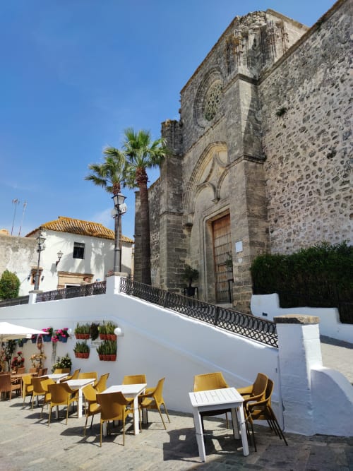 Terraza exterior con sillas amarillas en Casa De La Cruz Vejer, España, con vistas a la histórica iglesia de piedra