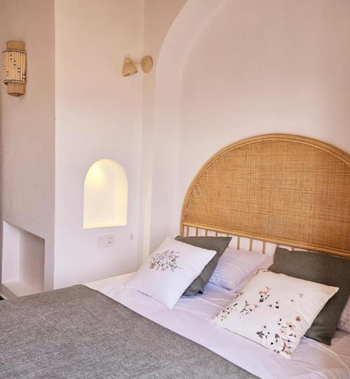 Dormitorio luminoso en Casa De La Cruz Vejer con cabecero de ratán tejido, ropa de cama blanca y ventana de alcoba arqueada en tonos rosados