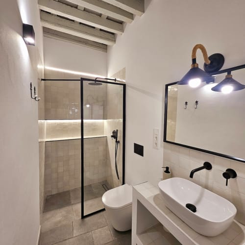Baño moderno de Casa De La Cruz Vejer con doble lavabo blanco, accesorios negros, ducha con mampara de cristal y piso de azulejos.