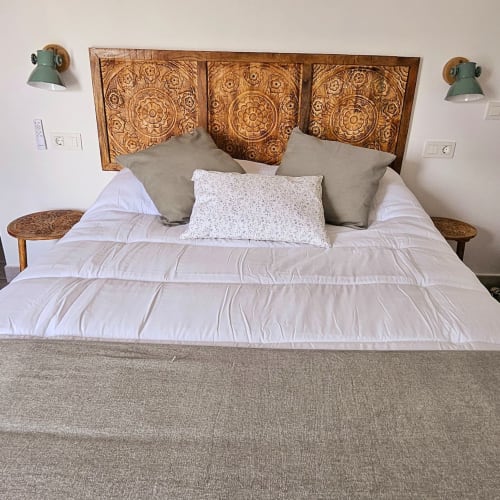 Dormitorio con cabecero de madera tallada, ropa de cama blanca, almohadas grises y apliques verdes en Casa De La Cruz Vejer