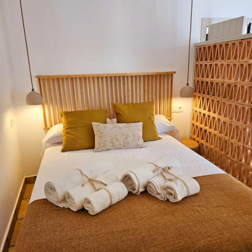 Habitación elegante en Casa De La Cruz Vejer con cabecero de madera, almohadas mostaza, toallas enrolladas e iluminación cálida