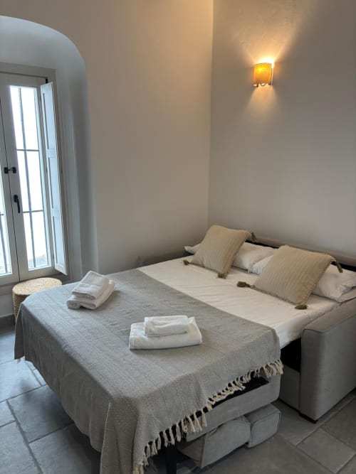Dormitorio de estudio en Casa De La Cruz Vejer con sofá cama, toallas dispuestas, puerta arqueada y aplique de luz cálida