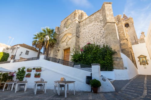 Patio de Casa De La Cruz en Vejer con iglesia de piedra, edificios encalados, mesas de comedor y palmeras