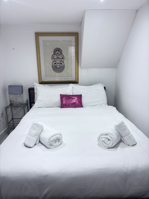 Modern bedroom with white bedding, rolled towels, purple cushion, and framed artwork at England Furnished Homes