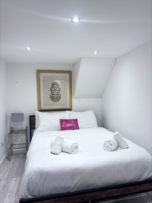 Modern attic bedroom in High Wycombe with white bedding, rolled towels, framed artwork, and recessed lighting