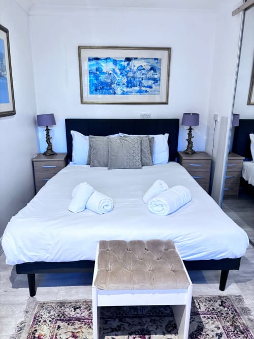 Modern bedroom at England Furnished Homes with queen bed, purple lamps, and blue landscape artwork in High Wycombe