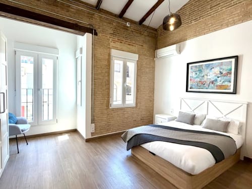 Dormitorio moderno en Stay Gest Valencia con paredes de ladrillo, suelos de madera, cama de matrimonio y acceso a balcón
