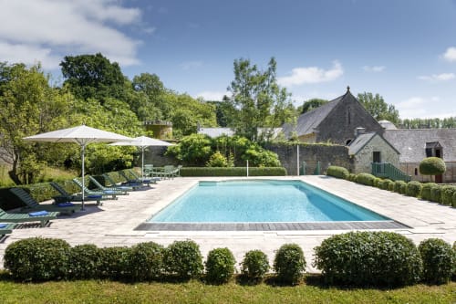 Piscine de luxe du Château de Servigny avec chaises longues, parasols et bâtisses en pierre à Yvetot Bocage, France