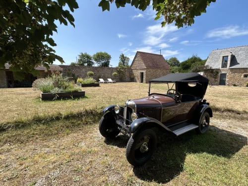 Voiture vintage exposée dans la cour du Sous Le Phare B&B, Louannec, France, avec bâtiments historiques en pierre