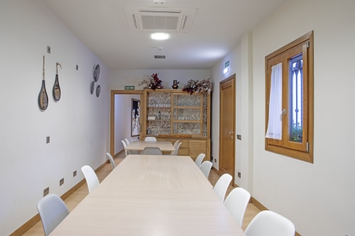 Sala da pranzo di Casa Azcona a Zizur Mayor con tavolo lungo, sedie bianche, armadi in legno e decorazioni murali