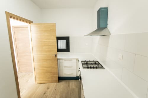 Cocina moderna del hotel DakarByDays con estufa de gas, campana extractora, gabinetes blancos y puerta de acceso de madera