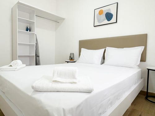 Modern bedroom at DakarByDays apartment in Dakar with white bedding, tan headboard, shelving unit, and abstract wall art