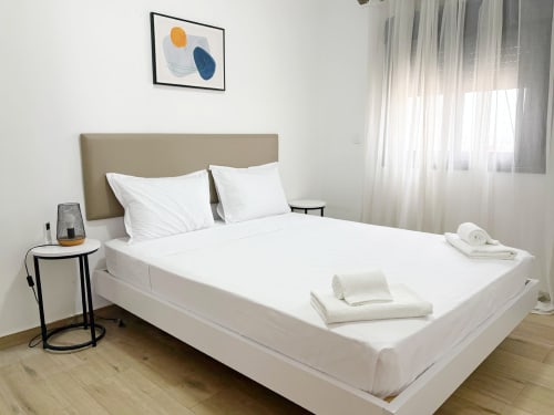 Modern bedroom with white linens and towels at DakarByDays apartment in Dakar, featuring beige headboard and city view