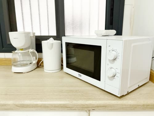 White kitchen appliances in DBD901 apartment: coffee maker, water dispenser, and microwave on wooden counter at DakarByDays