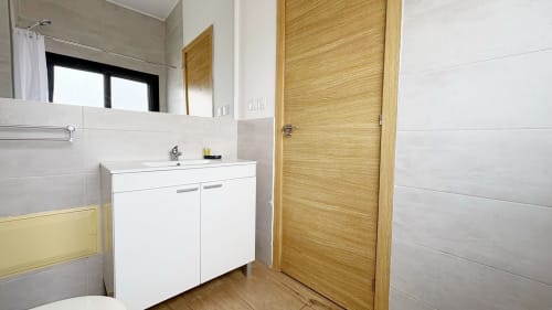 Modern bathroom in DakarByDays apartment with white vanity, wooden door, and tiled walls
