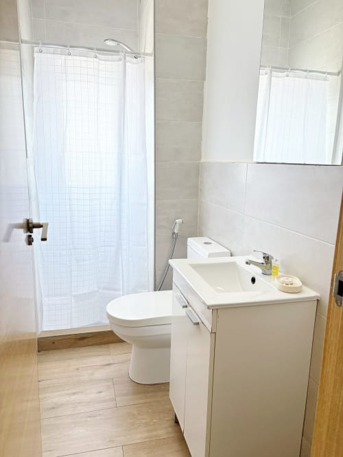 Modern bathroom in DakarByDays apartment with white toilet, sink vanity, shower with curtain, and wood-look flooring