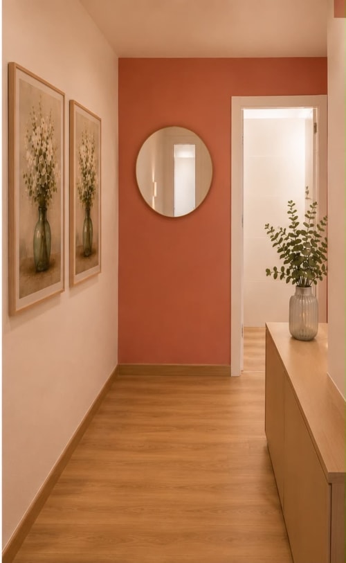 Modern hallway at Principe David Toledo apartment with terra cotta accent wall, round mirror, botanical artwork, and wooden