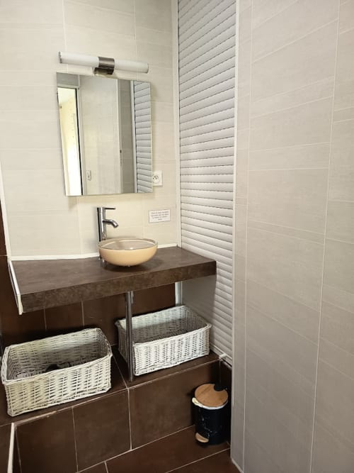 Salle de bain moderne avec vasque, miroir et paniers de rangement en osier à la Maison D'hôtes Coeur D'hérault à Péret