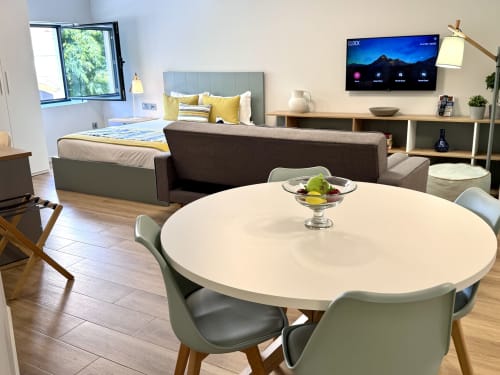 Appartement Premium Bleu au RIA CENTRUM avec salon ouvert, table à manger ronde blanche, canapé gris et lit jaune
