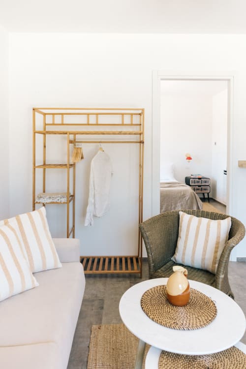 Modern apartment living room at Tenuta Fascianello with striped pillows, rattan chair, and wooden wardrobe rack in Fasano.