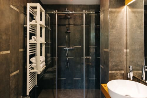 Modern bathroom at Tenuta Fascianello with walk-in shower, dark tile, white heated towel rack, and white sink.