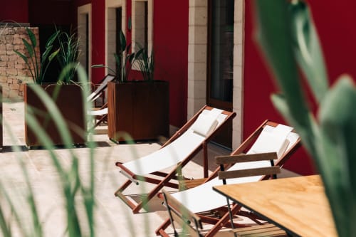Relaxation area at Tenuta Fascianello with wooden loungers, potted plants, and red-walled courtyard in Fasano