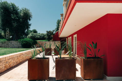 Red-walled modern apartment patio at Tenuta Fascianello in Fasano with potted plants, wooden planters, and garden views