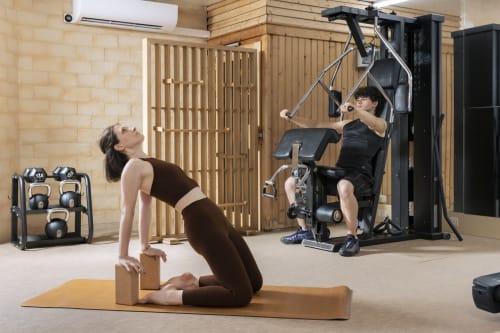 Studio de fitness moderne à l'Hôtel Residence Europe & Spa avec une femme pratiquant le yoga et un homme utilisant des équipements de musculation