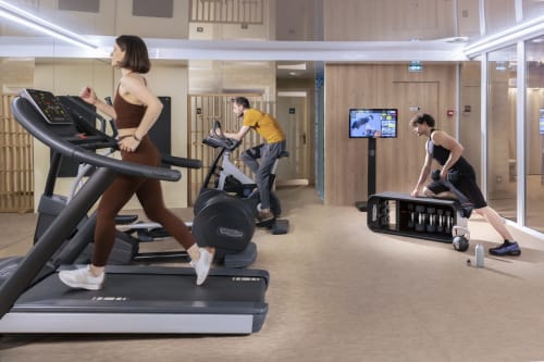 Centre de fitness moderne de l'Hôtel Residence Europe & Spa à Clichy avec des clients utilisant un tapis roulant, un vélo stationnaire et des poids
