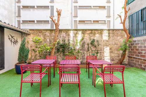 Vibrant red furniture and pink tables in Hotel Residence Europe & Spa's Clichy courtyard with artificial turf