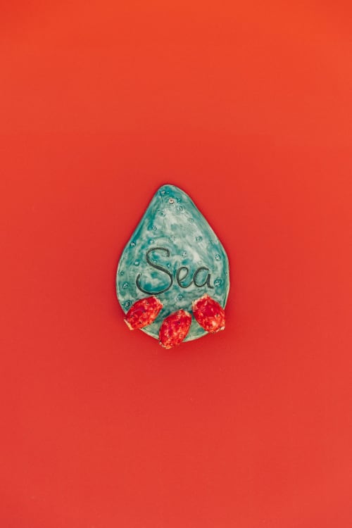 Turquoise ceramic shell with 'Sea' text and red strawberries on coral background, Tenuta Fascianello Fasano