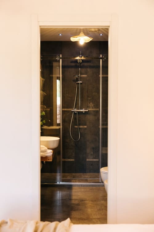Modern bathroom with walk-in shower, dark tile walls, and elegant brass fixtures at Tenuta Fascianello in Fasano