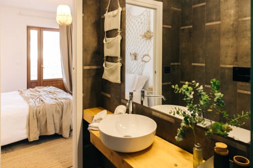 Luxury bathroom at Tenuta Fascianello with round white sink, dark tile walls, garden view, and bedroom access in Fasano