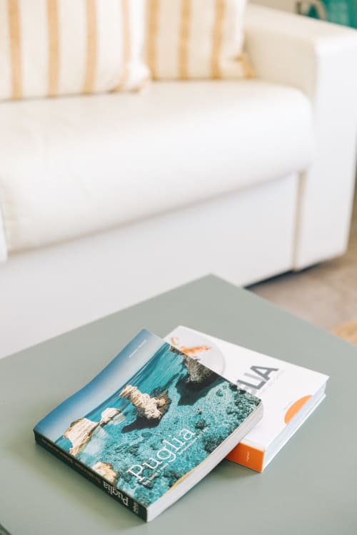 Travel guides on a green table beside a white upholstered sofa in a bright Fasano apartment interior