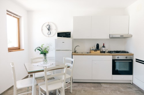 Modern white kitchen with wooden countertop in Fasano apartment, featuring dining area with fresh flowers